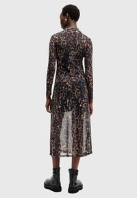 Μακρύ μανίκι φόρεμα με λεοπάρ μοτίβο από διαφανές ύφασμα, με ψηλό λαιμό και χωρίσει στο στρίφωμα. Συνδυάζεται με μαύρες μπότες μέχρι τον αστράγαλο με λεπτομέρειες από αγκράφα.