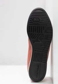 Semelle d'une chaussure en cuir marron avec une bande de roulement en caoutchouc noir texturé présentant des motifs géométriques et la marque « EMPORIO ARMANI ».