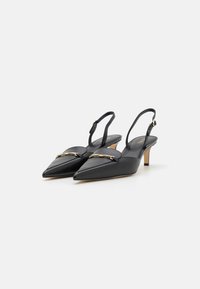 Chaussures à lanières en cuir noir avec un bout pointu, un talon bas et un accent doré à l'avant. Texture lisse et design minimal.