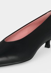 Chaussure femme en cuir noir à petit talon, bout arrondi et doublure intérieure rose sur un fond clair uni.