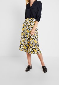 Geel en zwart dierenprint midi-jurkje met een flared silhouet, gecombineerd met een donkere blouse en zwarte loafers. Soepele stoftextuur.