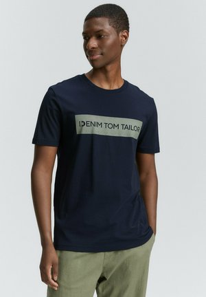 Temno modra kratka majica s kratkimi rokavi, ki vsebuje svetlo sivo pravokotno logotipno tiskanje z napisom "DENIM TOM TAILOR," postavljeno na gladki teksturi.