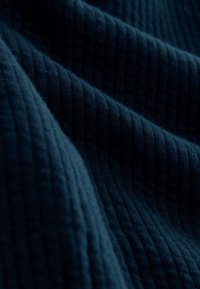 Tumma sininen resorikangas, jossa on pehmeä pinta ja hienovarainen kiilto. Kangas on koristeltu pystysuorilla linjoilla, jotka muodostavat aaltoilevan kuvion.