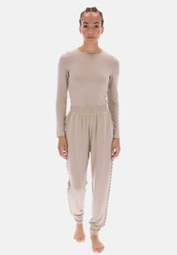 Beige langærmet top og matchende joggingbukser lavet af blødt materiale. Bukserne har bølget sidesøm og elastik i taljen.