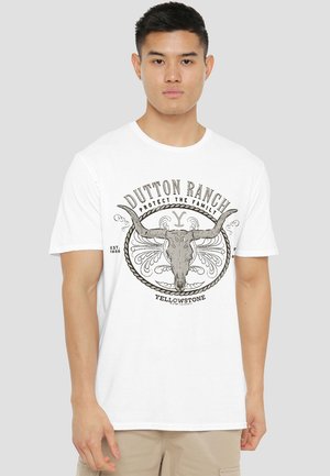 White cotton t-shirt featuring a graphic design of a bull skull with decorative elements and the text "Dutton Ranch" and "Yellowstone."
