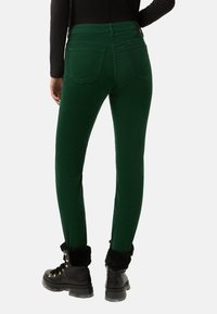 Zelené manšestrové kalhoty s přiléhavým střihem, dvěma zadními kapsami a vysokým pasem, doplněné černými bojovými botami s kožíškem.