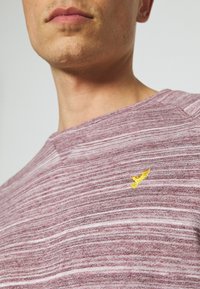 Felpa a righe bordeaux con scollo rotondo, presenta un piccolo logo di uccellino ricamato giallo sul petto. Tessuto morbido con un design casual.