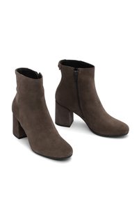 Botas de tobillo de ante marrón con tacones de bloque y cremalleras laterales, situadas sobre un fondo blanco.