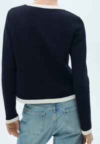 Pull-over bleu marine avec une bordure blanche au niveau de l'encolure et de l'ourlet, fabriqué en tissu texturé, associé à un jean en denim bleu clair.