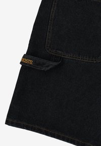 Czarna dżinsowa tkanina z kontrastującym żółtym szwem, z dużą przednią kieszenią i detalem z etykietą na boku.