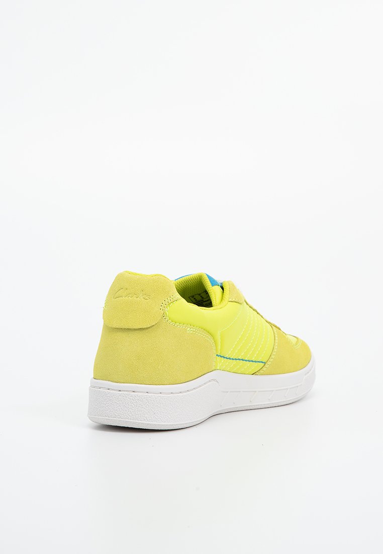 Zapatillas amarillas que combinan materiales lisos y texturizados, con una suela blanca y costuras de acento. La parte trasera muestra elementos de marca y diseño.