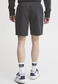Grå idrettsshorts med elastisk midje, baklomme og sidespalter, kombinert med hvite sokker med "BLEND" og hvite og marineblå sneakers.