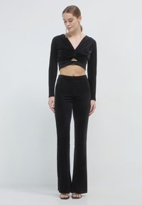 Completo due pezzi in velluto nero, composto da un crop top a maniche lunghe con fronte torcigliata e pantaloni palazzo a vita alta. Tessuto morbido e design aderente.