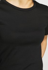 Camiseta negra de manga corta hecha de una suave tela elástica, con un cuello redondeado y una textura lisa sin patrones ni adornos visibles.