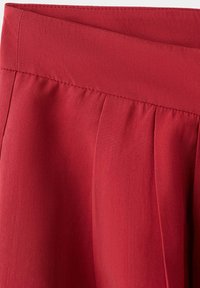 Jupe en tissu rouge avec une large ceinture et des plis cousus créant une texture subtile et une forme.
