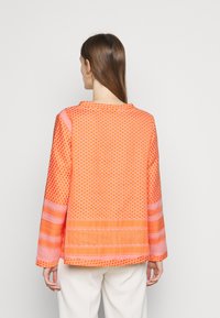 Blusa arancione con motivo a lungo maniche, caratterizzata da design geometrici e strisce orizzontali in diverse sfumature di arancione e rosa. Texture morbida.