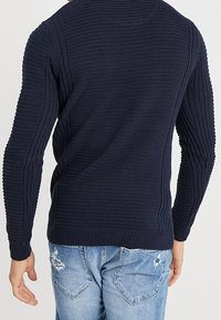 Pull en tricot côtelé bleu marine, coupe ajustée. Présente des motifs texturés horizontaux et verticaux, des manches longues et un col rond.