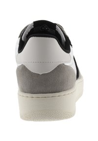 Baskets en cuir blanc avec des accents en daim noir et un talon gris. Forme arrondie, semelle en caoutchouc texturée, et coutures sur le dessus.