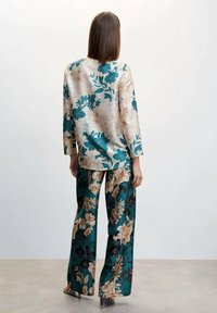 Satin-Outfit mit floralem Muster, bestehend aus einem cremefarbenen Oberteil mit türkisfarbenen und braunen Blumen sowie passenden weit geschnittenen Hosen, dargestellt an einem Modell von hinten.