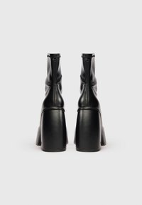 Botas de cuero negras hasta el tobillo con un alto tacón cuadrado, que presentan una textura suave, cierre de cremallera y un detalle de costura mínima.