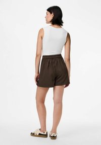 Top bianco senza maniche e pantaloni corti a righe marroni con vita elasticizzata. Le scarpe presentano un motivo a mucca con accenti di colore chiaro.