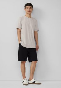 T-shirt gris clair à col rond et manches courtes, associé à un short noir et des baskets blanches avec des accents noirs et gris.