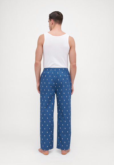Pantalons de pyjama bleus pour hommes avec des motifs de polos blancs, taille élastique et coupe ample. Portés avec un débardeur blanc.