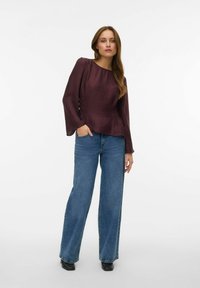 Bourgognefarvet tekstureret bluse med lange, udvidede ærmer kombineret med højtaljede blå vide jeans og sorte støvler med hæl. Enkel design.