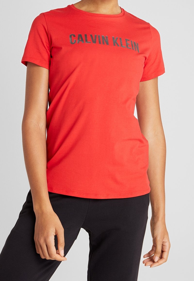 Rød bomulds T-shirt med korte ærmer og rund halsudskæring, med et sort "CALVIN KLEIN" logo over brystet. Glat tekstur.
