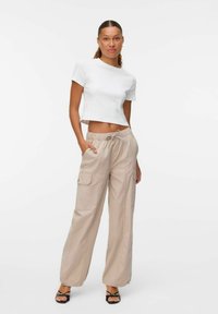 Wit cropped t-shirt gecombineerd met beige wijde cargobroek met zijzakken. Model draagt zwarte bandjes sandalen. Eenvoudig ontwerp en stof.