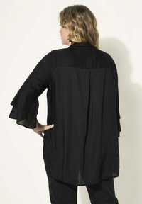Schwarze, locker sitzende Bluse mit Rüschenärmeln, aus leichtem Stoff gefertigt, mit rundem Kragen und einem leicht längeren hinteren Saum.