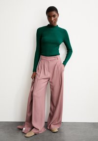 Groen geribd lange mouw top gecombineerd met hoge taille, wijde roze broek, met een knoopdetail bij de taille en een zachte stoftextuur.