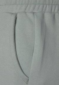 Ljusgrå sweatshirtmaterial med en sidficka, slät textur och resårmidja med synlig sömdetalj.