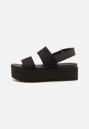 Sorte plattform sandaler i svart med to brede stoffstropper og justerbar ankelrem. Teksturert gummisåle, minimalistisk design.