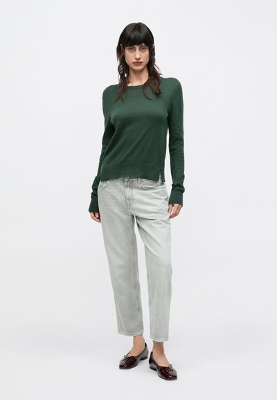 Πράσινο πλεκτό πουλόβερ με μακριά μανίκια, ανοιχτό γκρι τζιν παντελόνι με ίσια γραμμή και παπούτσια σε μπουρντό χρώμα. Το πουλόβερ έχει στρογγυλή λαιμόκοψη και πλαϊνές σχισμές.