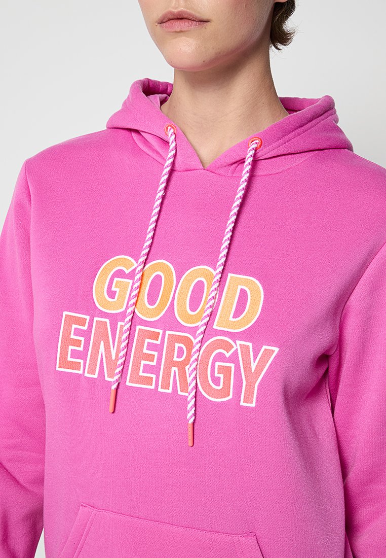 Rosa Kapuzenpullover mit "GOOD ENERGY" in Weiß und Orange bedruckt. Verfügt über eine Kapuze mit Zugschnürung und geflochtenen Details sowie eine vordere Kängurutasche.