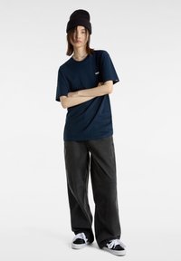 T-shirt en coton bleu marine à manches courtes avec un logo blanc, associée à un pantalon gris ample et des baskets noires avec des lacets blancs.