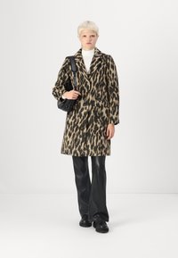Abrigo de estampado de leopardo en un tejido suave y texturizado; mangas largas, botones en la parte delantera, bolsillos laterales, combinado con pantalones y zapatos de piel negros.