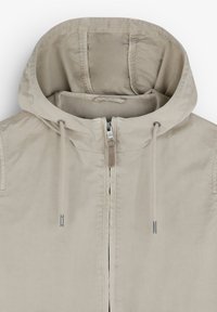 Giacca a vento beige chiaro con cappuccio, dotata di zip frontale, cordini sul collo e dettagli di cucitura sottili.