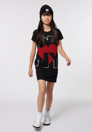 Robe T-shirt noire avec un graphique rouge et blanc "I ❤️ NY". Associée à un bonnet noir et des baskets montantes blanches. Design simple, manches courtes.