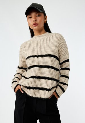 Beige gebreide trui met een textuurpatroon en zwarte horizontale strepen, met een ronde hals en een licht losse pasvorm.