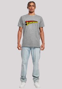 Grå bomull T-skjorte med en flerfarget "SUPERMAN" logo i fet skrift. Kombinert med lyseblå jeans og hvite joggesko.