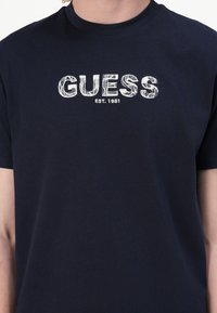 Námornícky modré bavlnené tričko s krátkymi rukávmi a okrúhlym výstrihom so bielym logom "GUESS" a textom "EST. 1981".