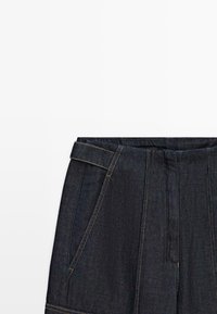 Short en denim bleu foncé avec poches avant, passants de ceinture et détails de couture visibles sur fond blanc.