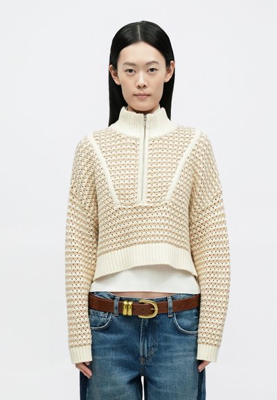 Pulover crem cropped cu guler înalt, având un design texturat cu ochiuri deschise și accente striate la tiv și la manșete.