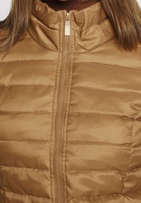 Brun dynejakke med vandret quiltet design, høj krave og lynlåslukning. Glat tekstur med blank finish.