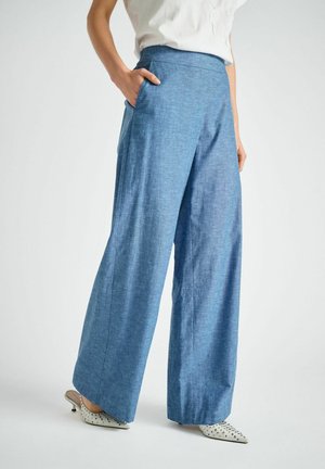 Lichtblauwe wijduitlopende broek met een gladde textuur, zijzakken en een hoge taille, gecombineerd met witte puntige schoenen met zwarte stippen.