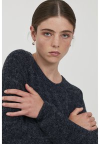 Pull en maille texturée bleu foncé, avec un col rond et des manches longues. Le tissu semble doux et pelucheux, renforçant la chaleur et le confort.
