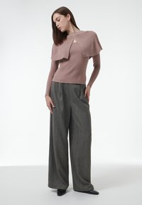 Rippenshirt in hellrosa mit langen Ärmeln und einem einzigartigen Überlagerungsdesign, kombiniert mit weiten, dunkelgrauen Hosen, die ein strukturiertes Muster aufweisen.