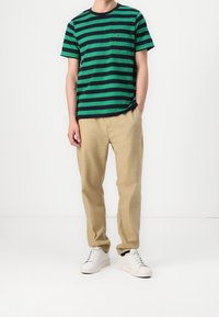 Raitapaitainen vihreä ja laivastonsininen t-paita etutaskulla, yhdistettynä beigeihin housuihin ja valkoisiin lenkkareihin. Yksinkertainen muotoilu, puuvillamateriaali.